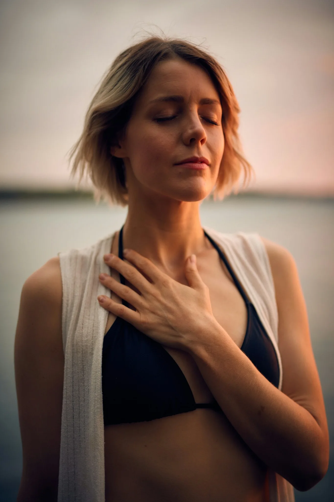 A woman pausing outdoors beside the water in warm evening light
